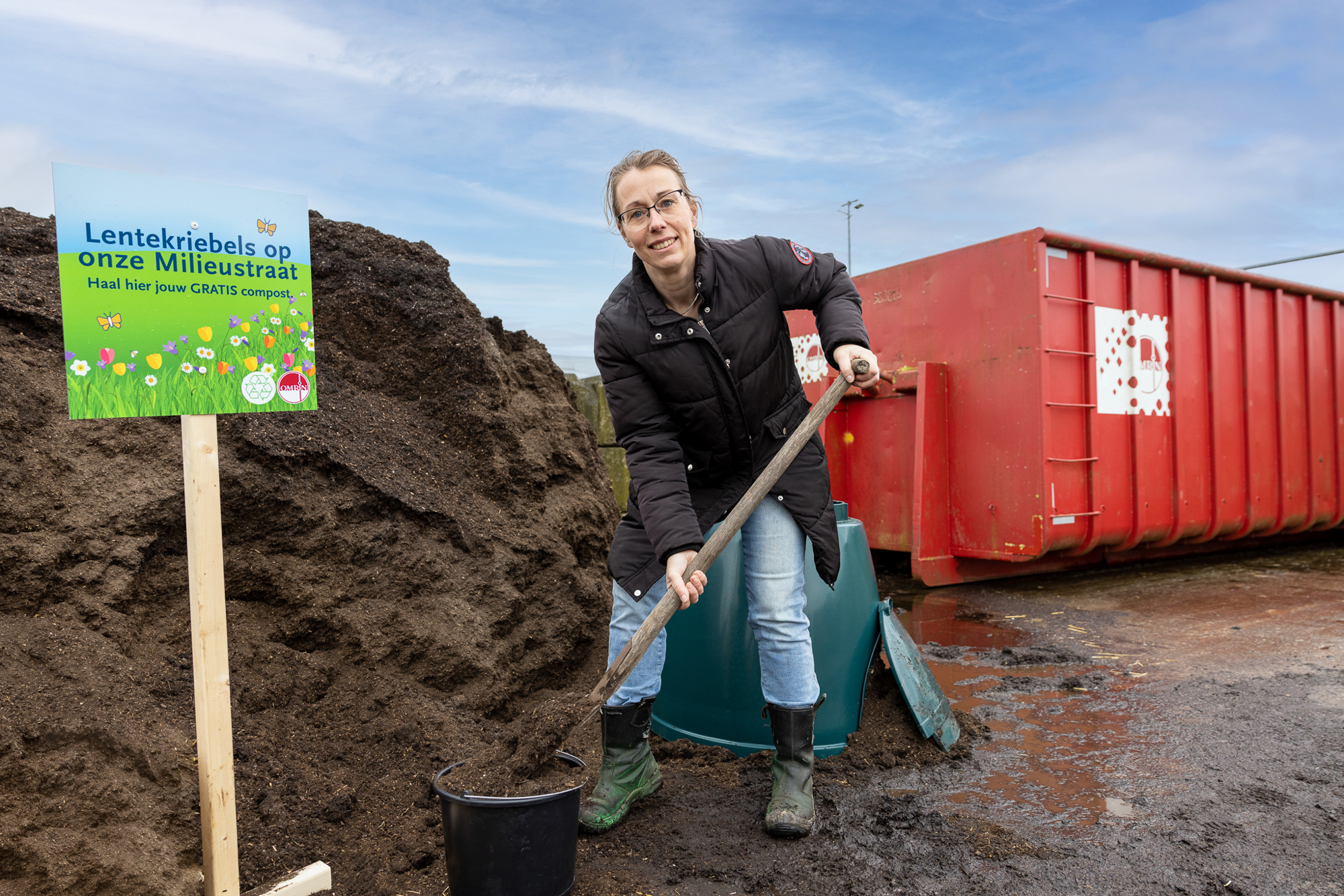 Vrouw op milieustraat schept compost in emmer