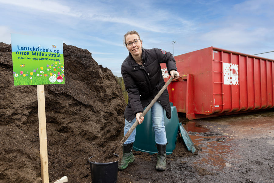 Vrouw op milieustraat schept compost in emmer